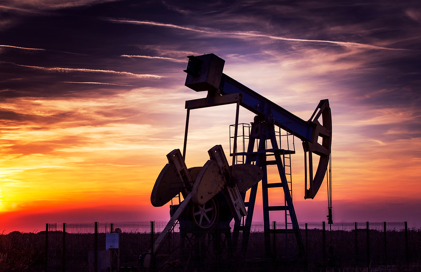 Oil pump jack silhouetted against dramatic sunset
